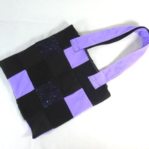 Peut inclure: Un sac fourre-tout en patchwork avec des carrés de tissu noir et violet. Le sac a une seule anse violette.