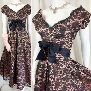 May include: A black and blush pink lace dress with a black satin bow at the waist. The dress has a sweetheart neckline and short sleeves.