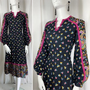 May include: Black long-sleeve dress with a floral and butterfly pattern. The dress features a V-neckline and pink trim along the collar, sleeves, and hem. The sleeves are long and puffy, and the dress has a midi length.