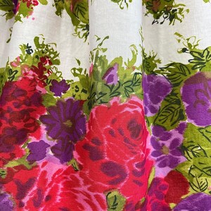 K&ouml;nnte beinhalten: Wei&szlig;er Stoff mit einem Blumendruck mit rosa, roten, violetten und gr&uuml;nen Blumen. Die Blumen sind stilisiert und haben einen malerischen Look.
