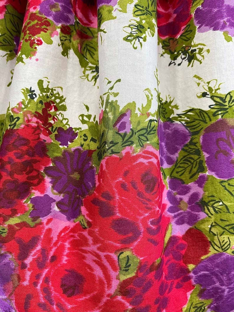 K&ouml;nnte beinhalten: Wei&szlig;er Stoff mit einem Blumendruck mit rosa, roten, violetten und gr&uuml;nen Blumen. Die Blumen sind stilisiert und haben einen malerischen Look.
