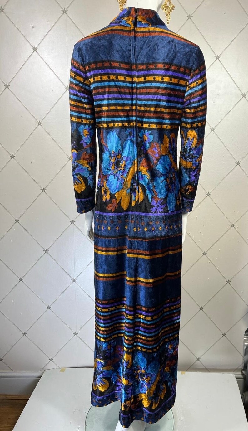 May include: A long blue velvet dress with a floral print and striped pattern. The dress has a high neck and long sleeves.