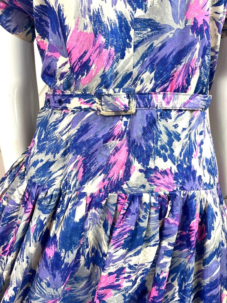 May include: A blue, pink, and white patterned dress with a fitted bodice and a full skirt. The dress has a belt at the waist.