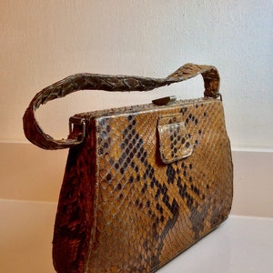 May include: A vintage brown and black snakeskin handbag with a silver clasp and a long strap.