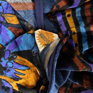May include: A blue and purple velvet fabric with a floral pattern and a yellow tag that says "Floral" with the word "Exclusive" underneath. The fabric has a zipper and a black metal pull.