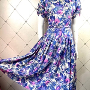 May include: A vintage floral dress with a white background and blue, pink, and purple abstract floral print. The dress has a sweetheart neckline, short sleeves, and a fitted waist with a belt.