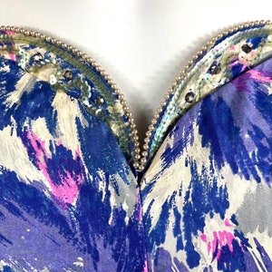 May include: A blue, pink, and white abstract print fabric with a beaded neckline. The neckline is adorned with iridescent sequins and small white pearls.