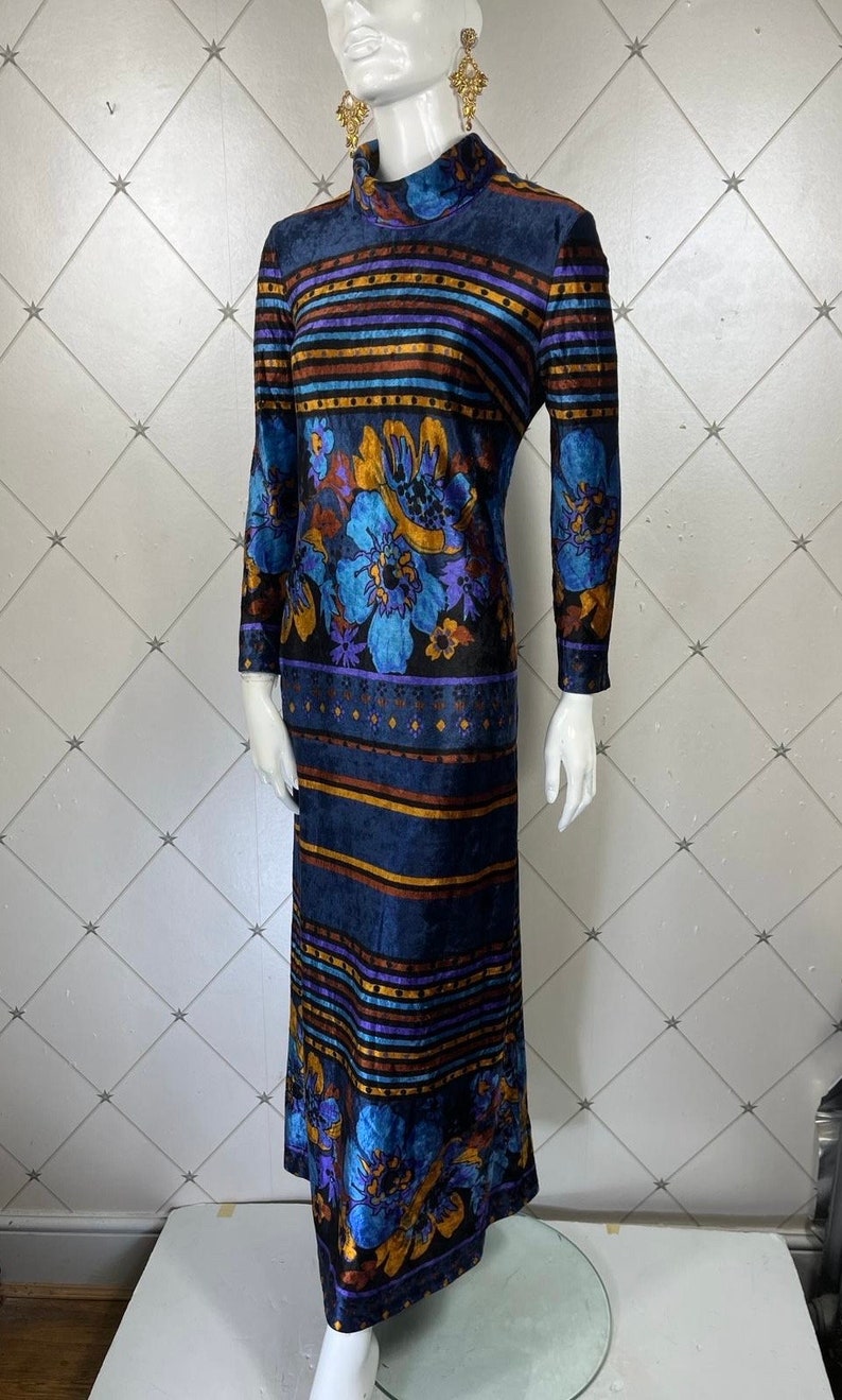 May include: A long-sleeved maxi dress with a high neck and a colorful floral and striped pattern. The dress is made of a soft, velvety fabric and has a fitted silhouette.