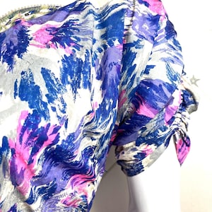 May include: A close-up of a white, blue, and pink patterned fabric with a gathered sleeve. The fabric has a swirling, abstract design.