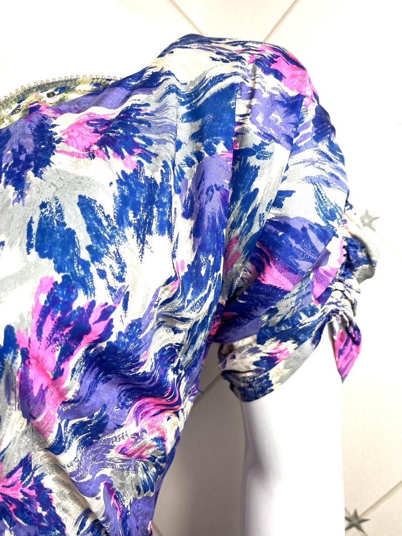 May include: A close-up of a white, blue, and pink patterned fabric with a gathered sleeve. The fabric has a swirling, abstract design.