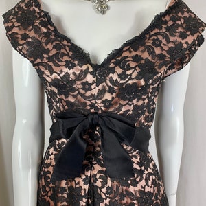 May include: A black and blush pink lace dress with a black satin bow at the waist. The dress has a V-neckline and short sleeves.