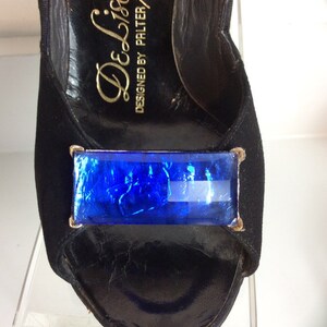 Puede incluir: Zapato de tac&oacute;n alto negro con punta abierta y un gran adorno rectangular de joya azul. El zapato est&aacute; hecho de ante y cuero, con letras doradas en el interior que dicen "De Liso Deb".