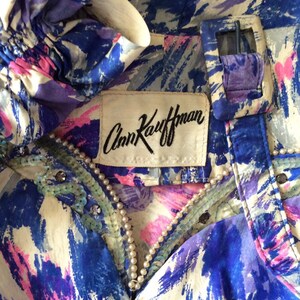 May include: A blue and white patterned silk blouse with a pearl and sequin trim. The blouse has a label that reads "Ann Kaufman".