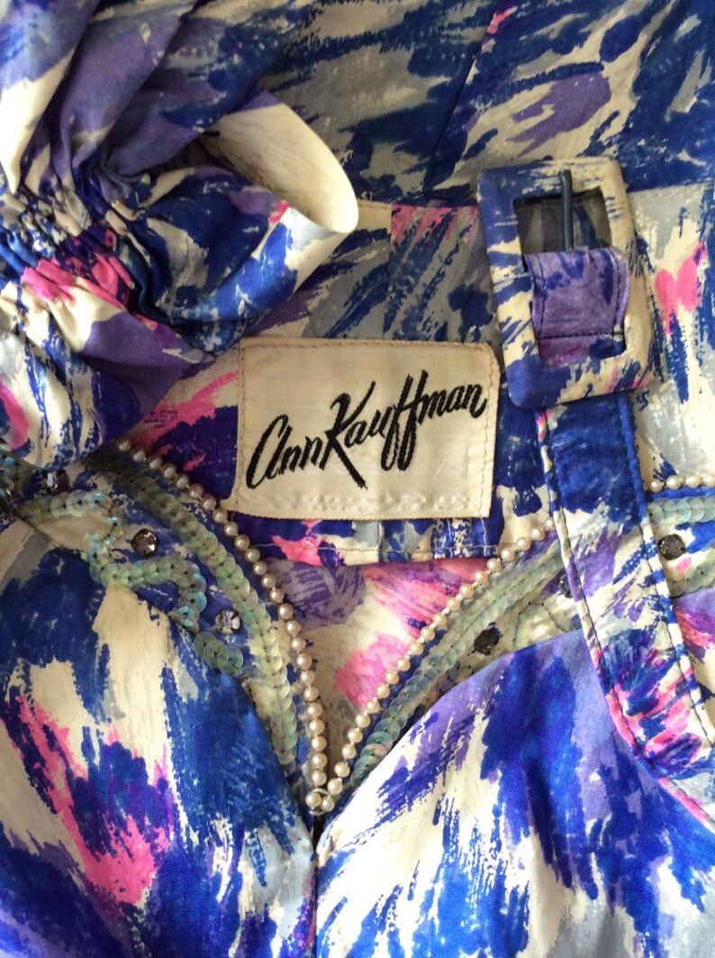 May include: A blue and white patterned silk blouse with a pearl and sequin trim. The blouse has a label that reads "Ann Kaufman".