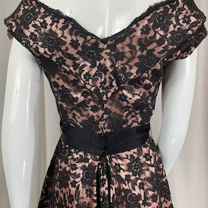 May include: A black lace dress with a pink lining and a black satin sash. The dress has a sweetheart neckline and short sleeves.