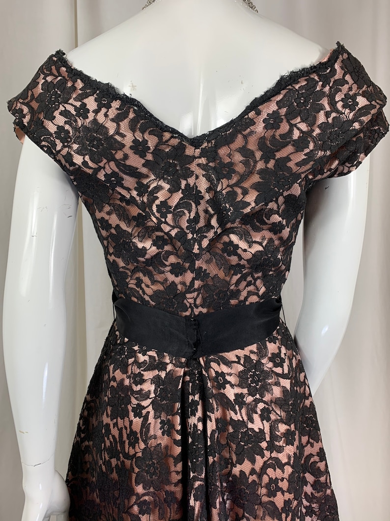 May include: A black lace dress with a pink lining and a black satin sash. The dress has a sweetheart neckline and short sleeves.