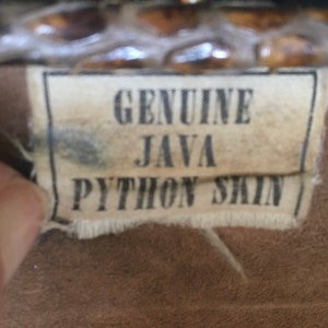 May include: Close-up of a brown leather tag with white stitching. The tag reads "GENUINE JAVA PYTHON SKIN".