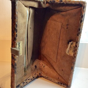 May include: Inside view of a vintage snakeskin handbag with a zippered pocket and a label that reads "Field". The bag has a brown suede lining and a small pocket on the opposite side of the zippered pocket. The label on the small pocket reads "Tailored  Exclusively for  Jay's".