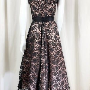 May include: A black lace dress with a pink lining and a black satin sash. The dress has a V-neckline and short sleeves.