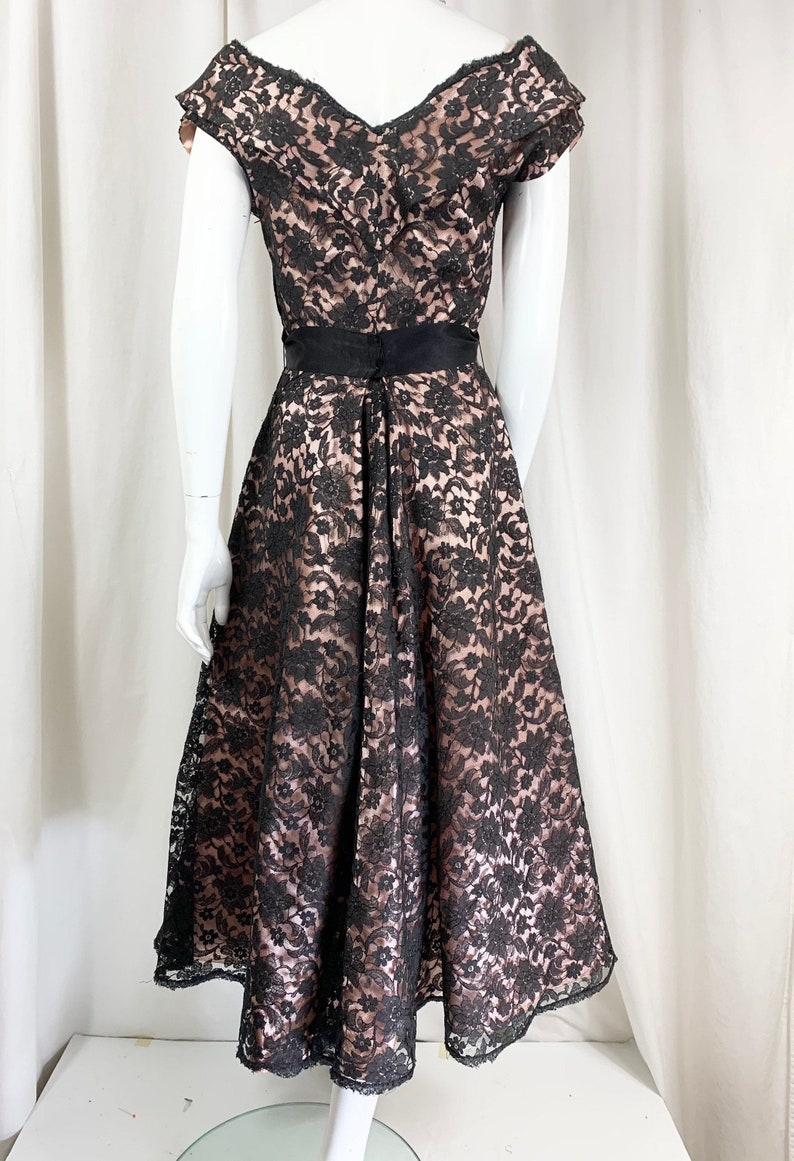 May include: A black lace dress with a pink lining and a black satin sash. The dress has a V-neckline and short sleeves.