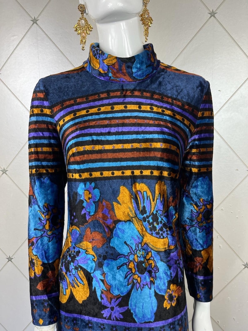 May include: A long-sleeved, high-necked dress with a blue, purple, orange, and brown floral pattern on a black background. The dress has a striped pattern around the neck and waist.