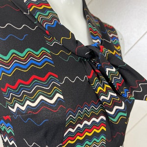 May include: A black sleeveless dress with a colorful wavy pattern. The dress has a tie at the neck.
