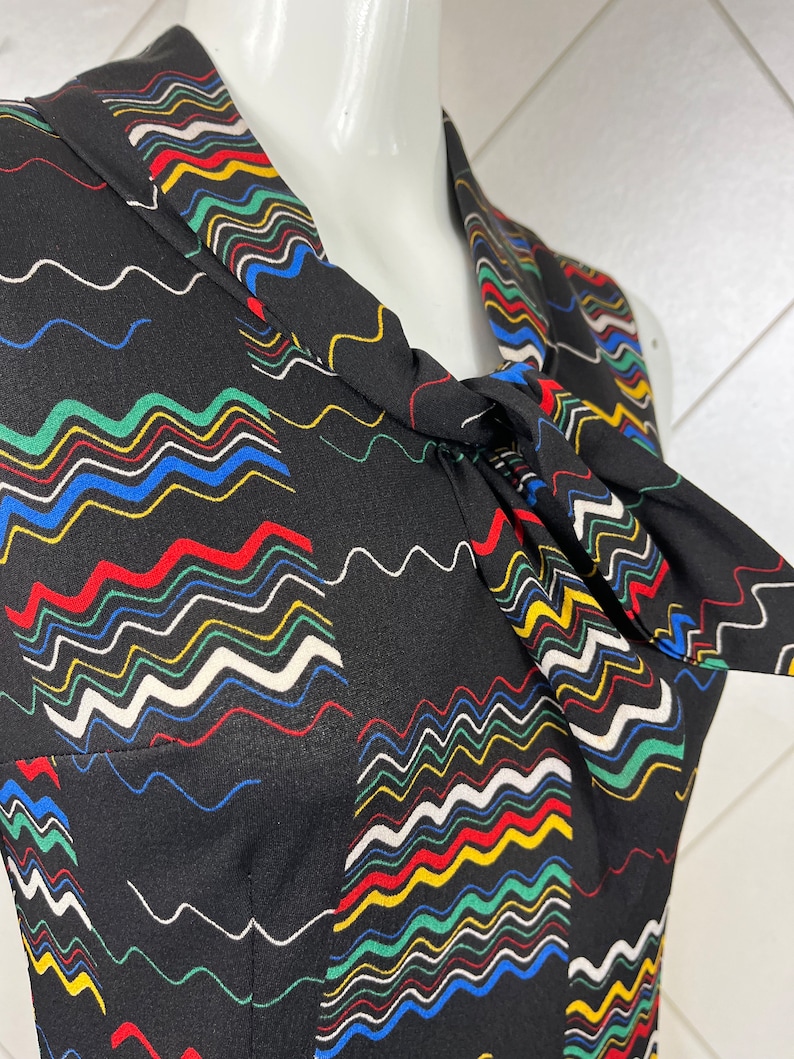 May include: A black sleeveless dress with a colorful wavy pattern. The dress has a tie at the neck.