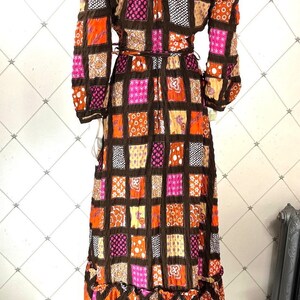 K&ouml;nnte beinhalten: Ein langes, schulterfreies Kleid mit Patchwork-Muster. Das Kleid ist aus braunem, orangefarbenem, rosa und gelbem Stoff. Der Stoff hat eine gesteppte Textur. Das Kleid hat lange &Auml;rmel und ein tailliertes Oberteil. Der Rock ist weit und flie&szlig;end.