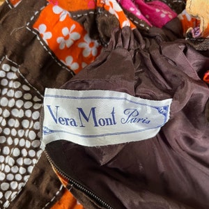 K&ouml;nnte beinhalten: Ein brauner Stoff mit wei&szlig;en Punkten und ein brauner Stoff mit wei&szlig;en Blumen. Der Stoff hat einen Rei&szlig;verschluss und ein Etikett mit der Aufschrift "Vera Mont Paris".