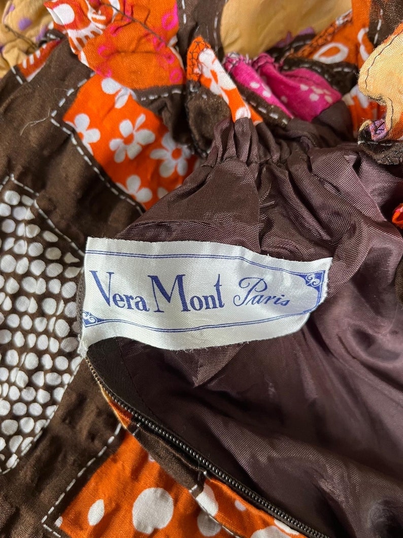 K&ouml;nnte beinhalten: Ein brauner Stoff mit wei&szlig;en Punkten und ein brauner Stoff mit wei&szlig;en Blumen. Der Stoff hat einen Rei&szlig;verschluss und ein Etikett mit der Aufschrift "Vera Mont Paris".