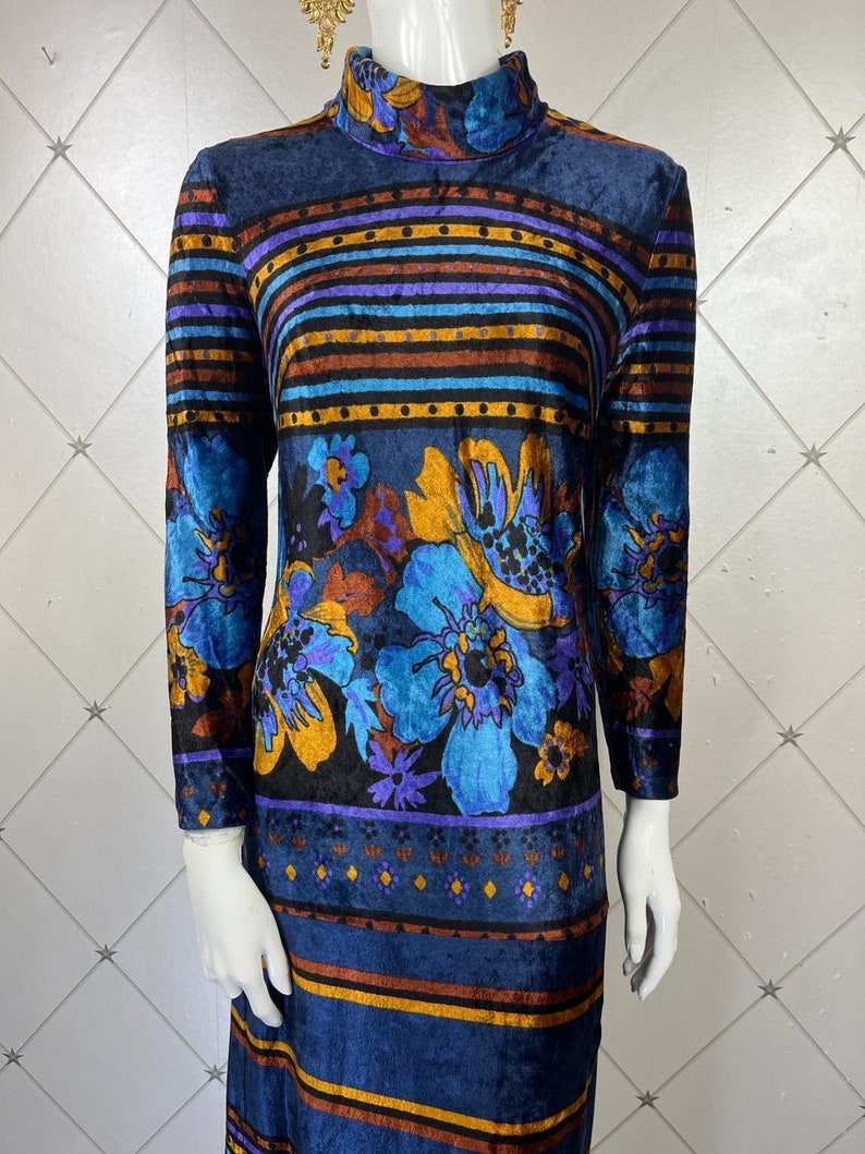 May include: A long-sleeved, blue velvet dress with a high neck and a colorful floral pattern. The dress has a striped pattern with brown, blue, and purple stripes.