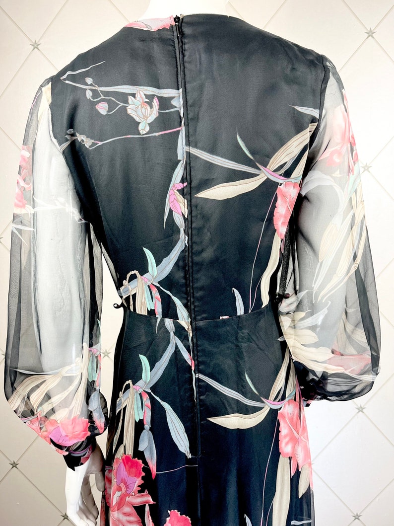 Peut inclure: Robe noire &agrave; imprim&eacute; floral avec manches longues transparentes. La robe pr&eacute;sente un motif floral aux tons rose, blanc et vert. Elle a un col montant et un corsage ajust&eacute;, avec une jupe fluide.