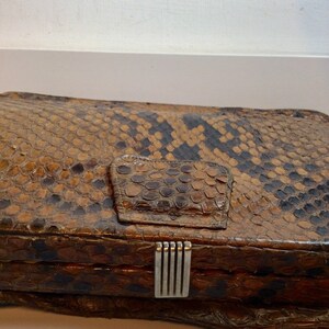 May include: A vintage brown snakeskin clutch purse with a silver clasp. The purse has a textured surface and a flap closure.