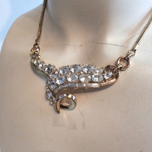 May include: A gold tone necklace with a large, clear rhinestone design. The design features a swirl with oval and baguette shaped rhinestones.