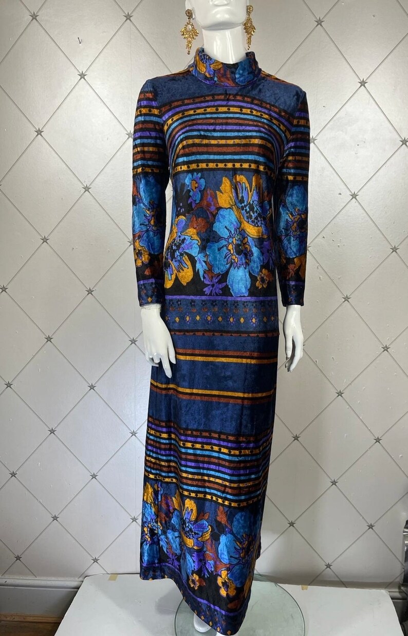 May include: A long-sleeved maxi dress with a high neck and a colorful floral and striped pattern. The dress is made of a soft, velvety fabric and has a relaxed fit.