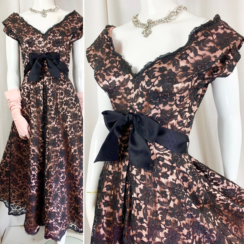 May include: A black and blush pink lace dress with a black satin bow at the waist. The dress has a sweetheart neckline and short sleeves.