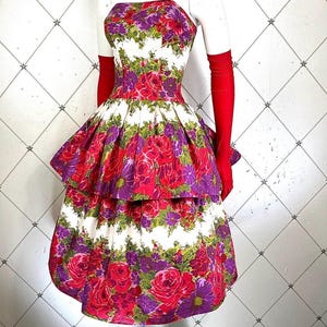 K&ouml;nnte beinhalten: Ein wei&szlig;es tr&auml;gerloses Kleid mit einem mehrfarbigen Blumendruck. Das Kleid hat ein tailliertes Oberteil und einen vollen Rock mit zwei Lagen. Das Kleid ist aus einem leichten Stoff gefertigt und hat einen Vintage-Stil.