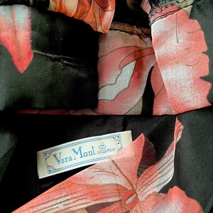 Peut inclure: Gros plan sur un v&ecirc;tement noir avec un motif floral dans les tons de rose, de rouge et de blanc. Le tissu est transparent et superpos&eacute;. Une &eacute;tiquette avec le texte "Vera Mont Paris" est visible.