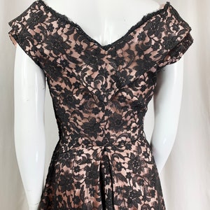 May include: A black lace dress with a sweetheart neckline and short sleeves. The dress is made of a sheer fabric with a floral pattern. The dress is fitted through the bodice and flares out at the skirt.