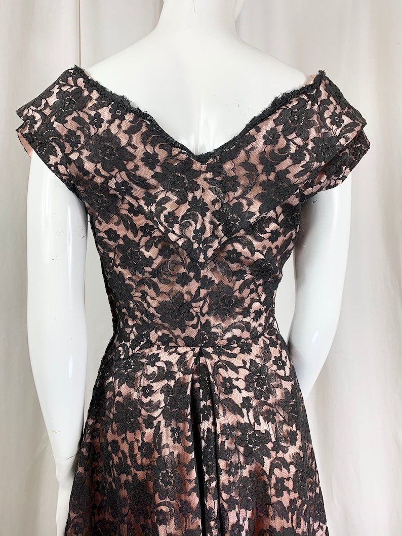 May include: A black lace dress with a sweetheart neckline and short sleeves. The dress is made of a sheer fabric with a floral pattern. The dress is fitted through the bodice and flares out at the skirt.