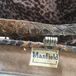 May include: Close-up of a brown leather purse with a silver clasp and a white label that reads "Mansfield".