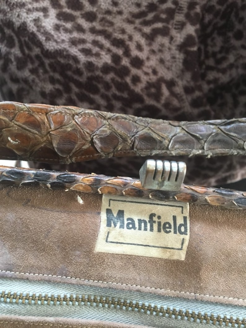 May include: Close-up of a brown leather purse with a silver clasp and a white label that reads "Mansfield".