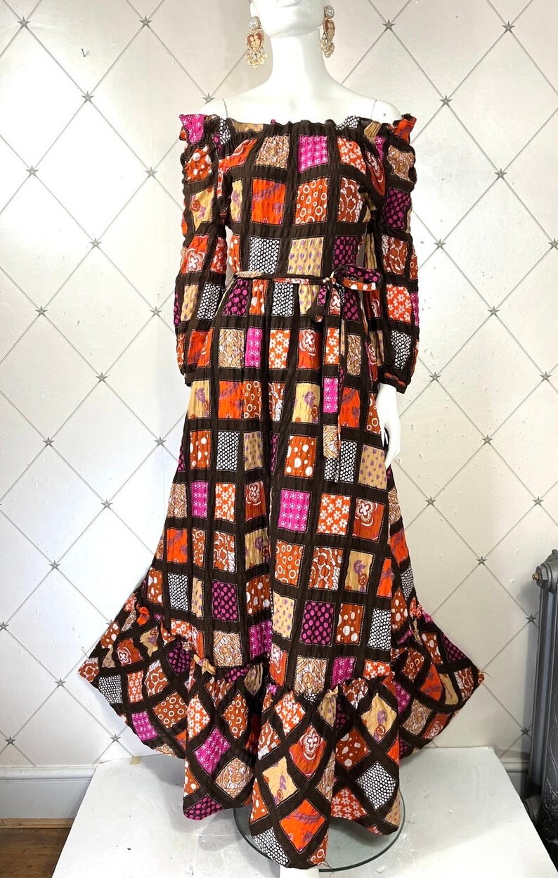 K&ouml;nnte beinhalten: Ein langes, schulterfreies Kleid mit Patchwork-Muster in Braun-, Orange-, Rosa- und Wei&szlig;t&ouml;nen. Das Kleid hat einen R&uuml;schen-Saum und eine Schleife in der Taille.