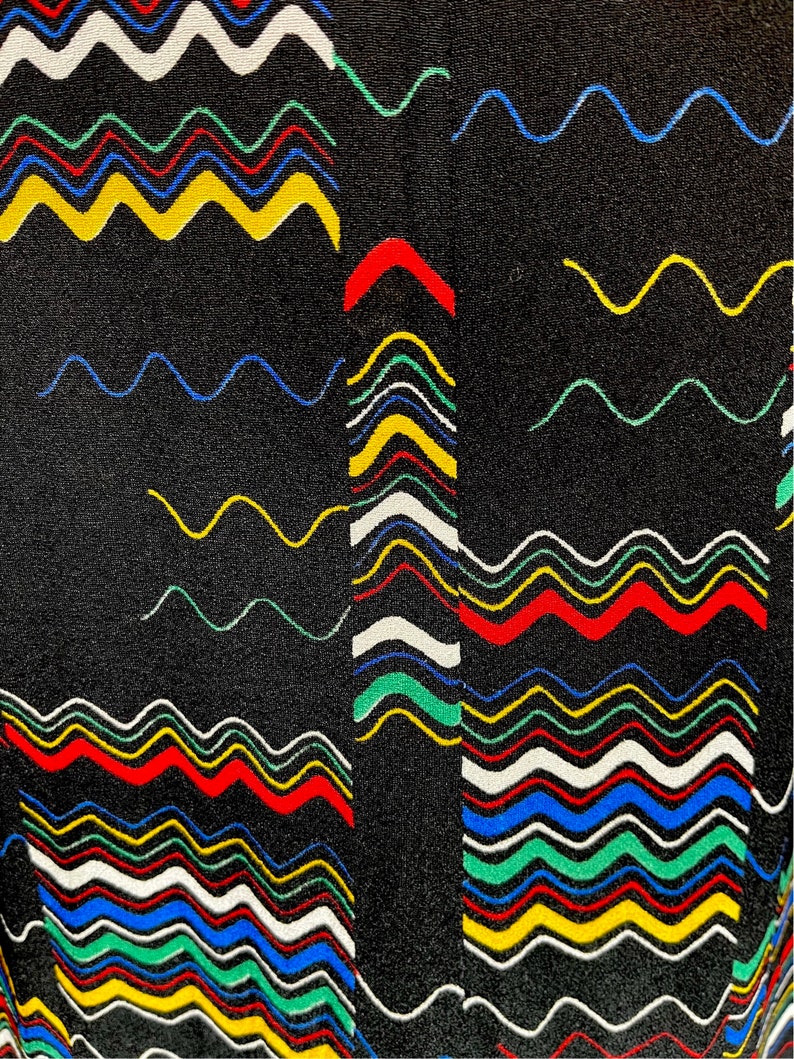 May include: Black fabric with a colorful wavy pattern. The pattern is made up of red, yellow, blue, green, and white wavy lines.