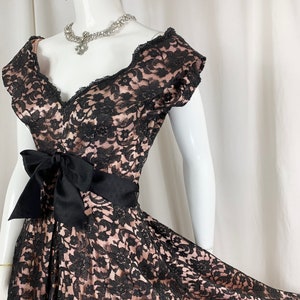 May include: A black and pink lace dress with a black satin bow at the waist. The dress has a sweetheart neckline and short sleeves.
