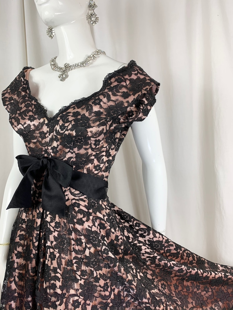 May include: A black and pink lace dress with a black satin bow at the waist. The dress has a sweetheart neckline and short sleeves.