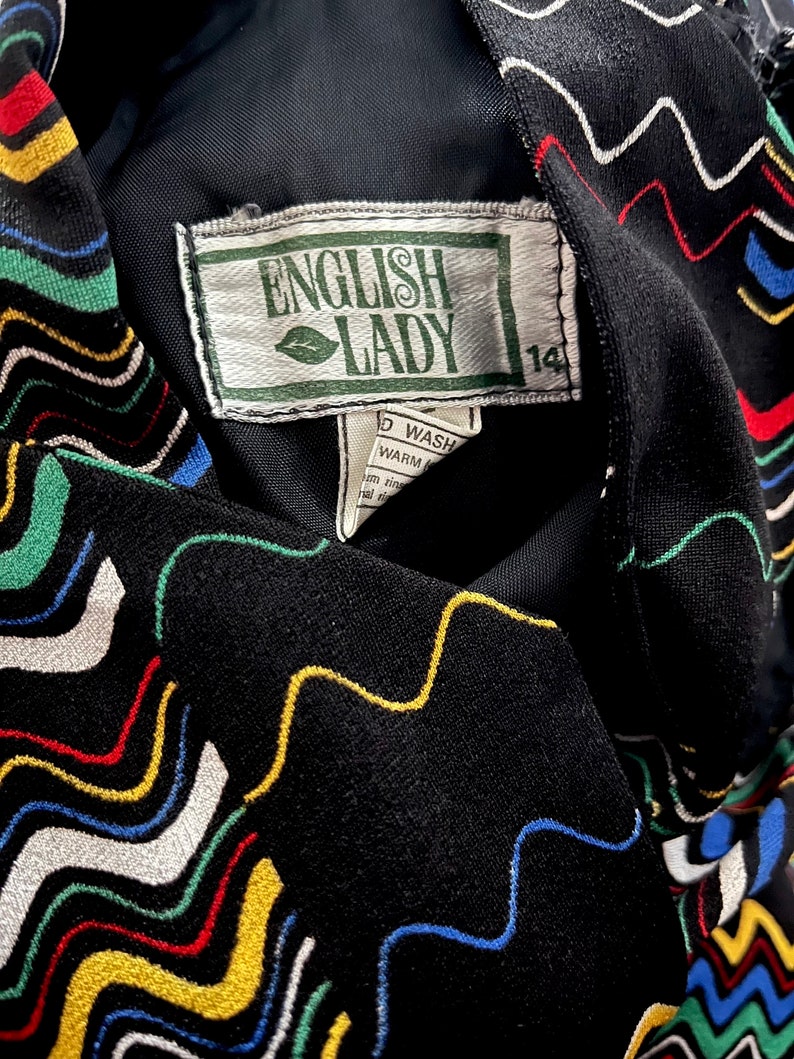 May include: Black fabric with a colorful wavy pattern and a white tag that says "English Lady" with a green leaf logo and the number "14" on it.