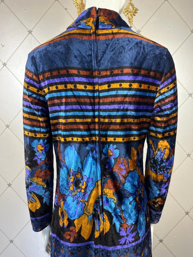 May include: A long-sleeved dress with a high neck and a zipper down the back. The dress is made of a dark blue velvet fabric with a colorful floral and striped pattern.
