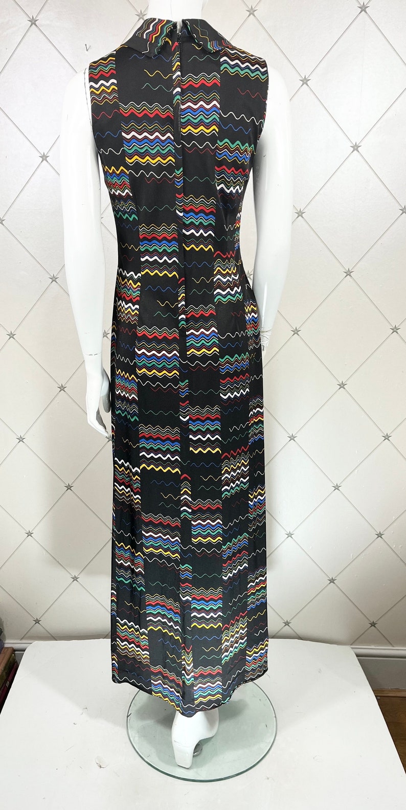 May include: A sleeveless maxi dress with a black background and a colorful wavy pattern. The dress has a collared neckline and a zipper closure in the back.