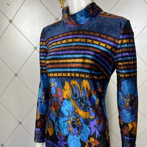 May include: A blue velvet dress with a multi-colored striped pattern and floral print. The dress has a high neck and long sleeves.